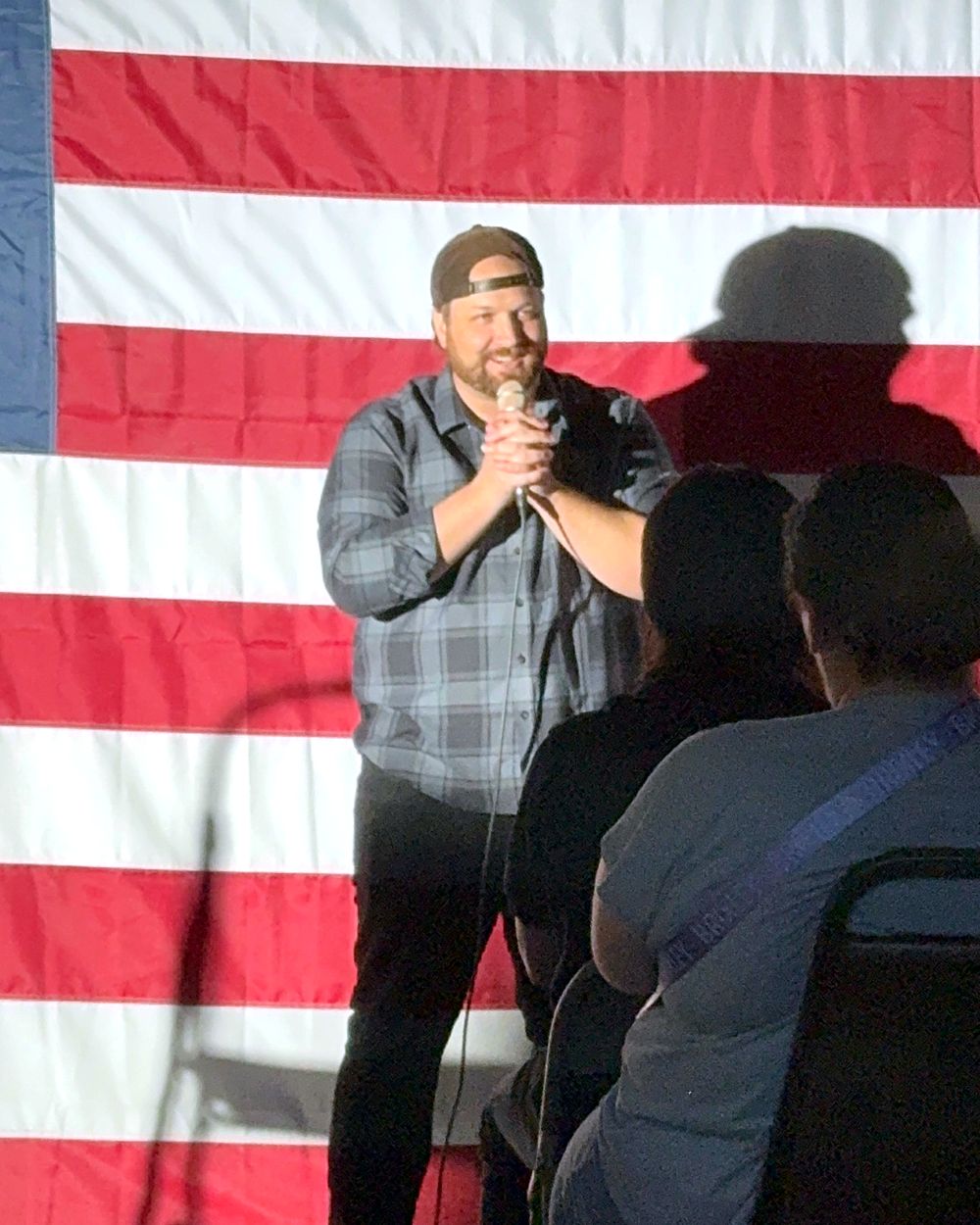 Jaron Wardle on stage with a microphone in front of an American flag