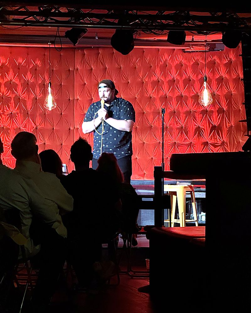 Jaron performing on a stage with a red tufted wall