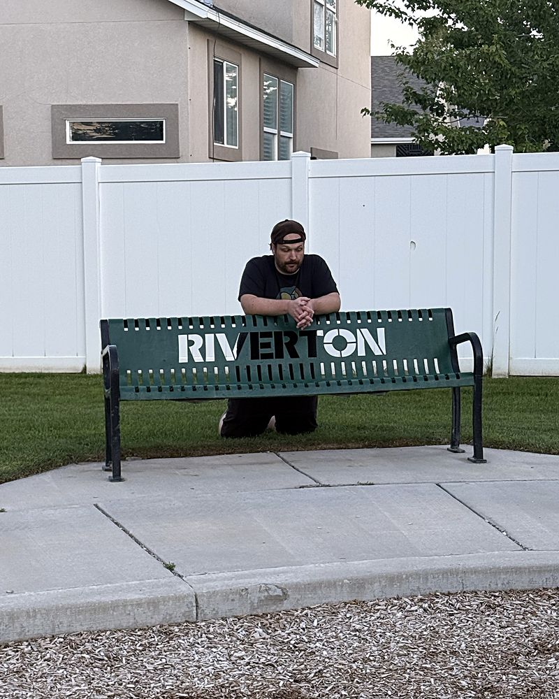 Jaron kneeling behind a green Riverton park bench, looking defeated