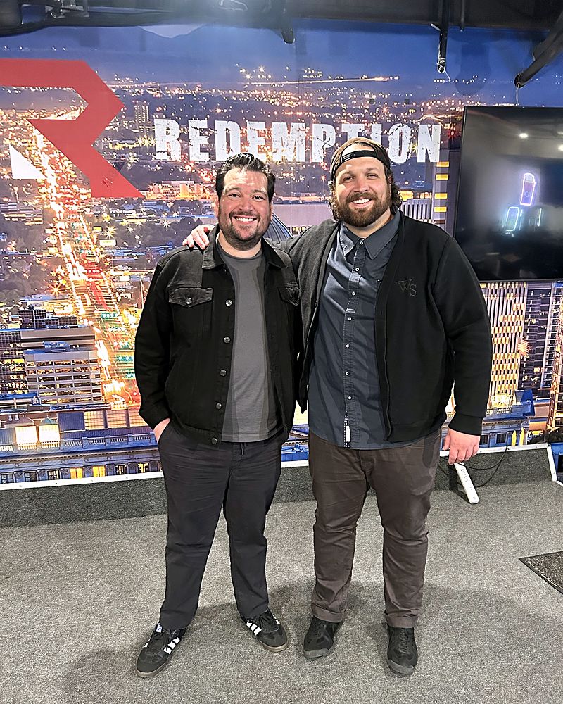Jaron and his co-host smiling in front of the Redemption mural